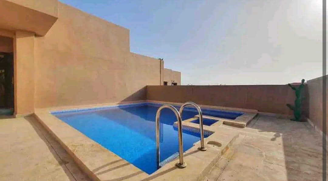 A rooftop terrace features a private swimming pool with clear blue water, complemented by a section for lounging. A smooth stone deck surrounds the pool area, providing ample space for relaxation. The distant horizon is visible under a bright sky, creating a serene atmosphere.
