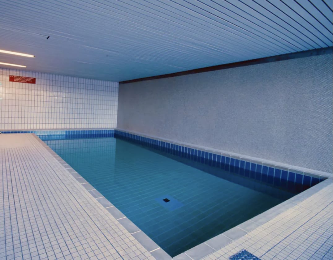 An indoor swimming pool is featured, with tiled walls and floors in various shades of blue. The tranquil water reflects the overhead lighting, creating a calming atmosphere.