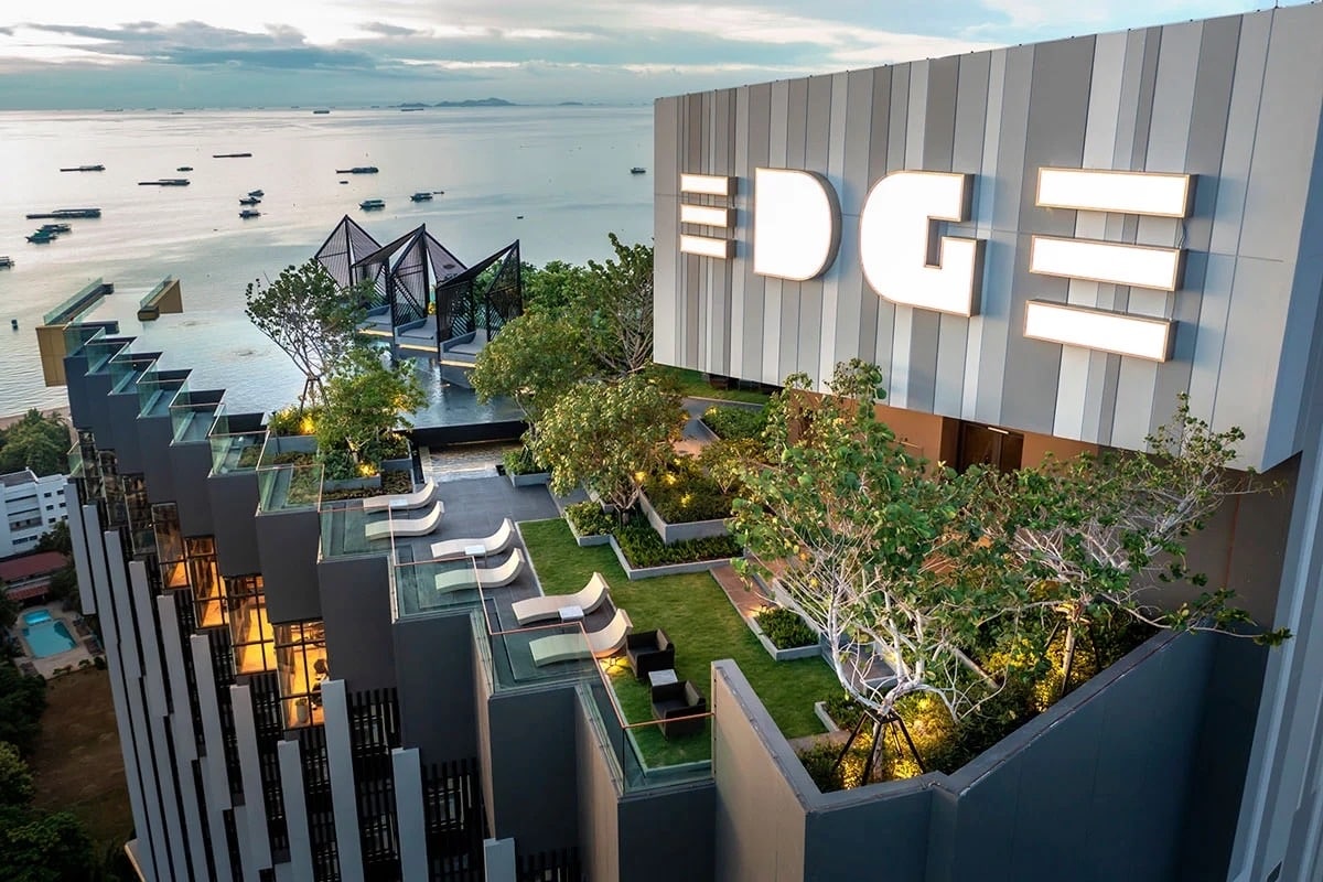 The rooftop area features a spacious terrace adorned with greenery and lounge seating, overlooking the ocean. The building's name, 'EDGE', is prominently displayed, enhancing the modern aesthetic. A panoramic view of the surrounding water adds to the inviting atmosphere of the space.