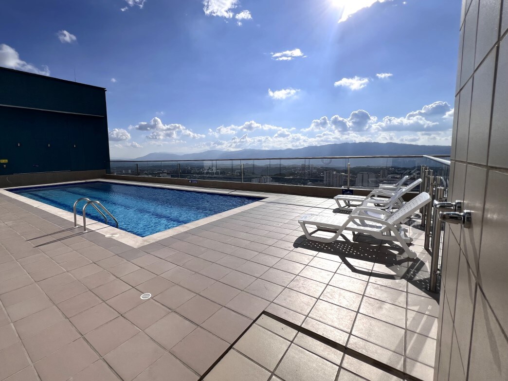A panoramic pool area is presented with a clear sky above, showcasing a rectangular swimming pool surrounded by a spacious deck. Several lounge chairs are arranged nearby, offering a place to relax while enjoying the view of the surrounding landscape.