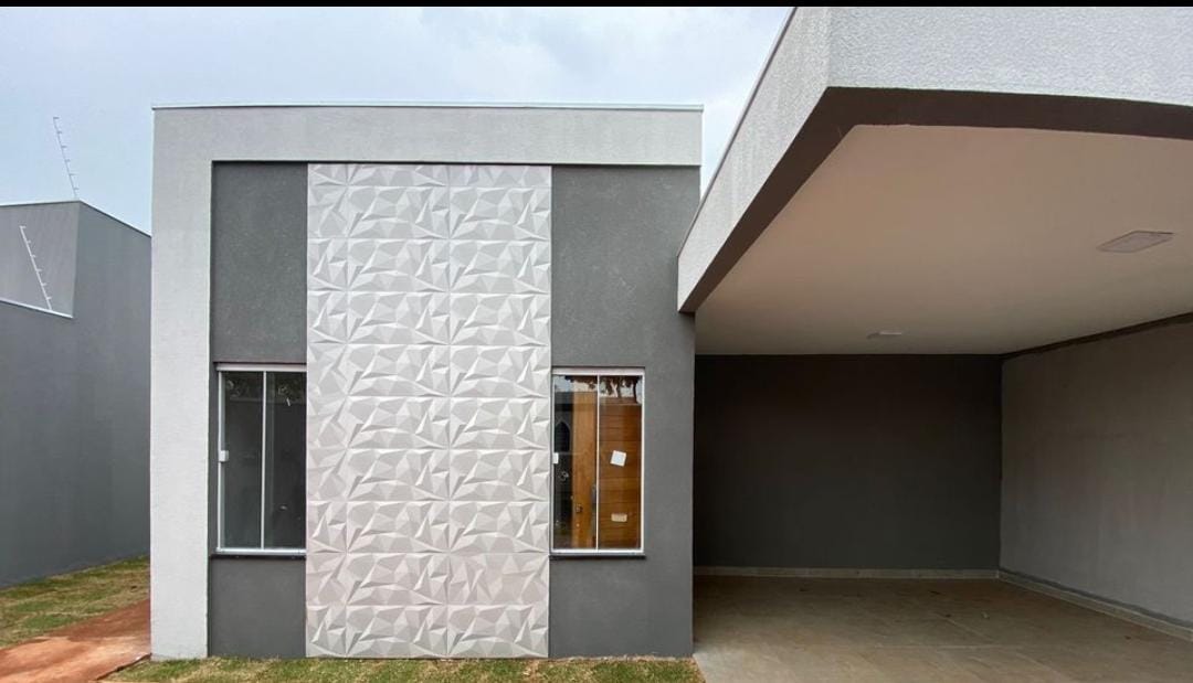 The modern exterior of the house features a geometric design on one wall, contrasting with the smooth gray finish of the other. Two large windows provide natural light to the interior, while a covered carport is accessible to the side.