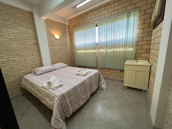 חדר שינה עם מיטת קינג סייז, חלון מיזוג אוויר ובריכה לשטיפת ידיים ופנים.