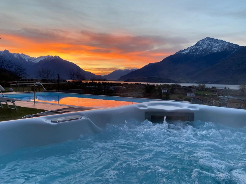 The image captures a warm sunset over a tranquil lake, with mountains in the background. A jacuzzi is displayed in the foreground, with bubbles gently rising. The scene is complemented by a pool reflecting the vibrant colors of the sky, creating a serene ambiance.