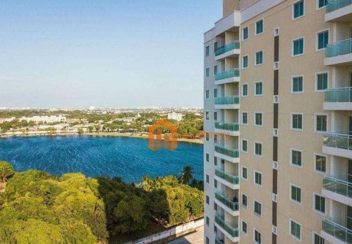 The image captures a panoramic view from the 13th floor, showcasing a large, tranquil lagoon bordered by lush greenery. The modern apartment building is seen on the right, featuring balconies and large windows that complement the natural scenery.