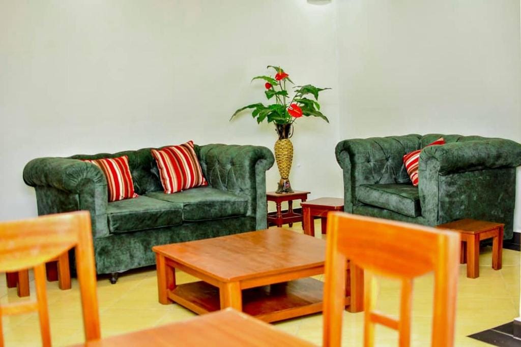 Two plush green sofas are positioned opposite each other, adorned with red and white striped cushions. A small wooden coffee table sits in between, complemented by a decorative plant in a woven basket, creating a relaxed seating area.