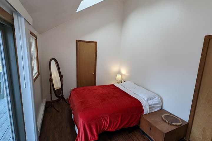 Sonniges Schlafzimmer mit einem Queensize-Bett, einem Oberlicht und einer privaten Terrassentür zum Deck. 