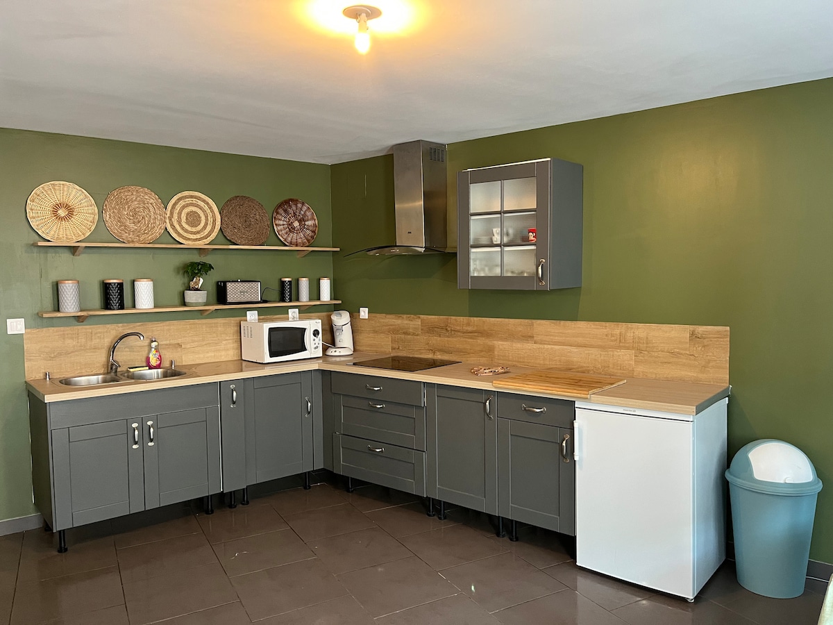 A modern kitchen features gray cabinetry and a light wood countertop. A microwave, refrigerator, and a sink are included. Decorative plates are displayed on the wall. The walls are painted a calming green, with tile flooring providing a clean appearance.