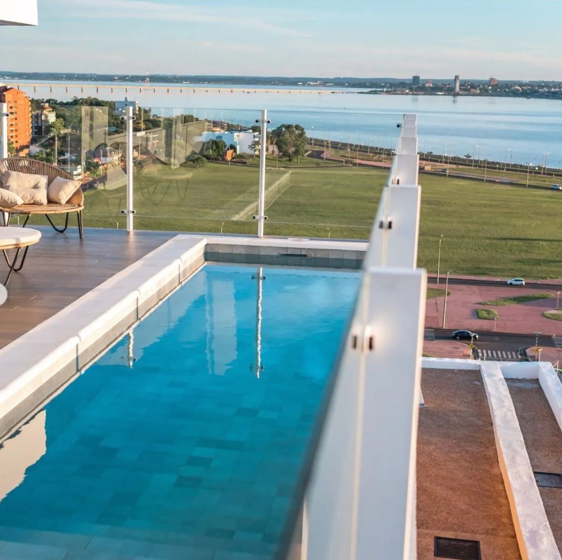 A private infinity pool is situated on a terrace, offering sweeping views of the water and landscape beyond. Glass railings provide unobstructed sightlines, enhancing the openness of the space. A lounge chair is positioned near the pool, inviting relaxation.