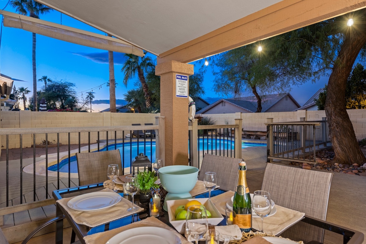 An outdoor seating area features a table set for dining, complete with plates and glasses. In the background, a private heated pool is visible, surrounded by palm trees and a tranquil atmosphere, showcasing a relaxing space for gatherings.