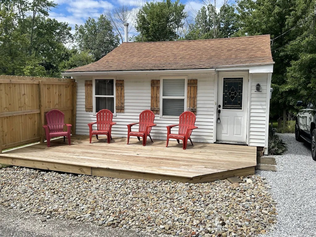The exterior of the home features a wooden deck with four red adirondack chairs, inviting relaxation. A white façade is complemented by wooden shutters on the windows. A gravel pathway leads to the entrance, with a wooden fence providing privacy.