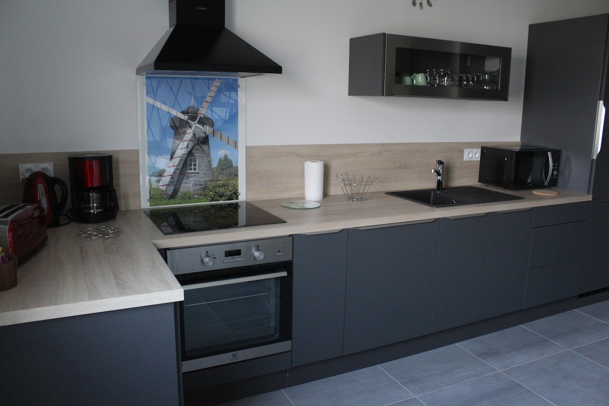 The kitchen features modern cabinetry in dark tones, complemented by a light wood countertop. An integrated stove and oven are present, along with a microwave and a coffee maker. A decorative mural of a windmill is visible on the wall behind the sink.