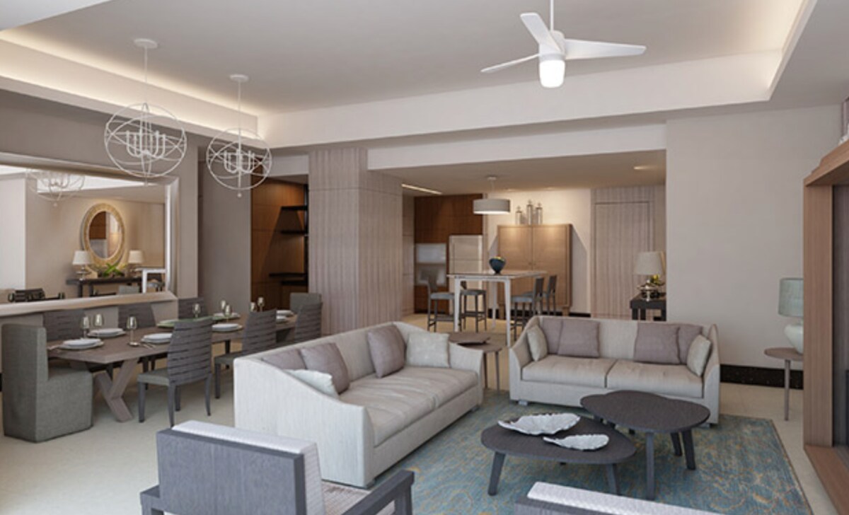 A spacious living area features modern furniture with two sofas and a coffee table, surrounded by natural light. An elegant dining space with a large table and multiple chairs is visible in the background. A sleek kitchen with minimalist cabinetry is also present.