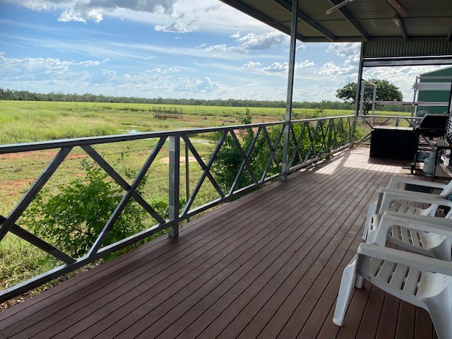 A spacious wooden deck features two white chairs, offering an unobstructed view of the surrounding landscape. Lush greenery and a distant horizon with scattered clouds create a serene backdrop. The railing's design adds a touch of elegance while ensuring safety.