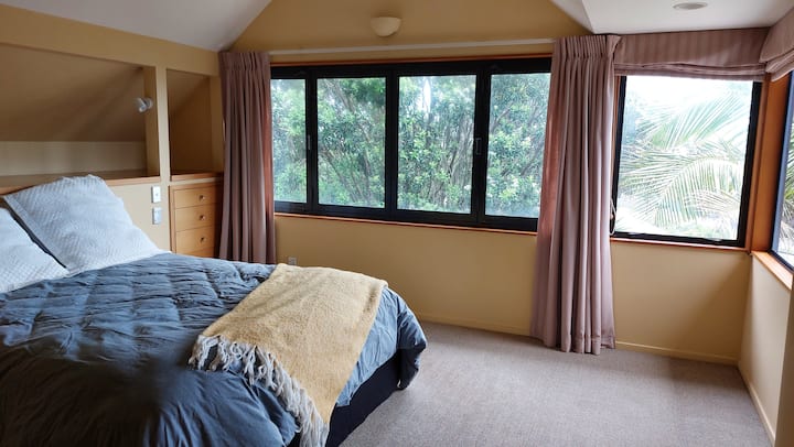 El dormitorio principal tiene vistas al mar y a la reserva, y un precioso pohutakawa fuera de las ventanas. 