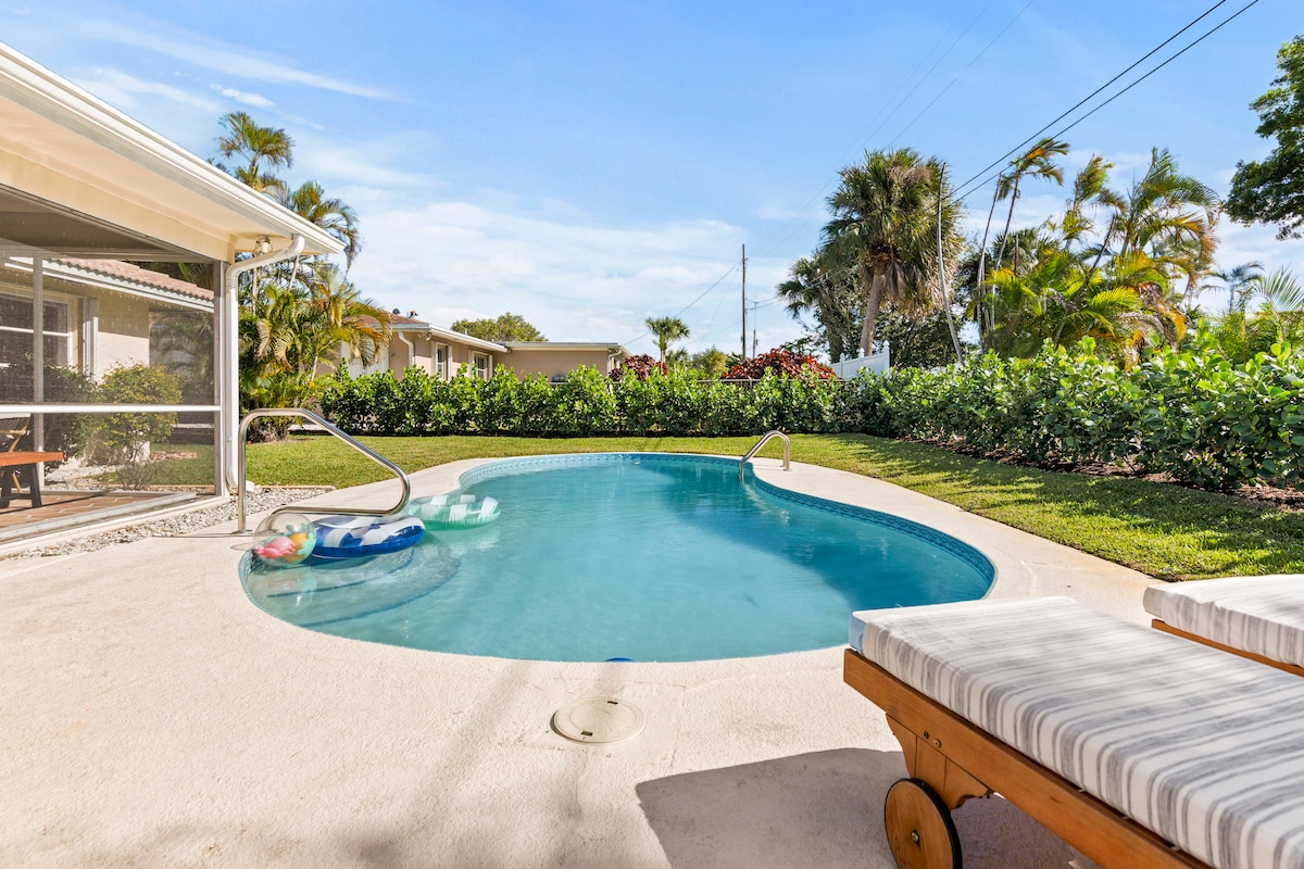 A refreshing swimming pool is framed by a spacious patio, featuring lounge chairs for relaxation. Lush greenery and tropical plants provide a natural backdrop, while the screened-in area offers a sense of privacy. The inviting water beckons for a dip on a sunny day.