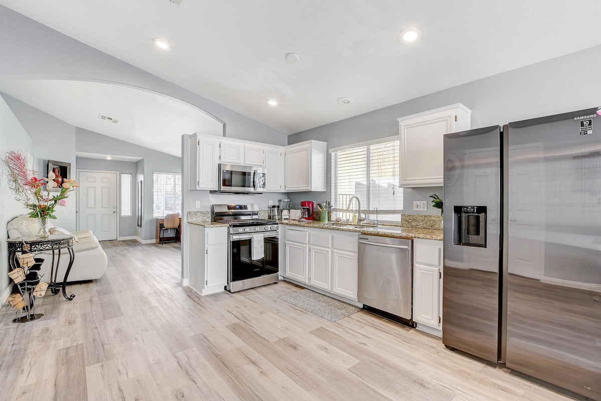 A spacious modern kitchen is highlighted by granite countertops and stainless steel appliances, including a refrigerator and microwave. The open layout allows light to fill the area, and laminate flooring extends throughout. A dining area is visible in the background, contributing to the home's inviting atmosphere.