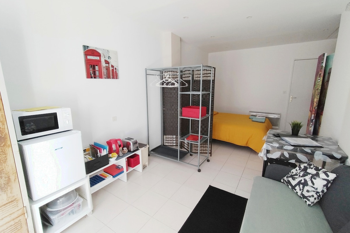 An open space includes a cozy sleeping area with a colorful bedspread, a kitchenette with a microwave, and a seating area outfitted with a couch. A decorative partition separates the sleeping area. Shelving and storage solutions are thoughtfully arranged for convenience.