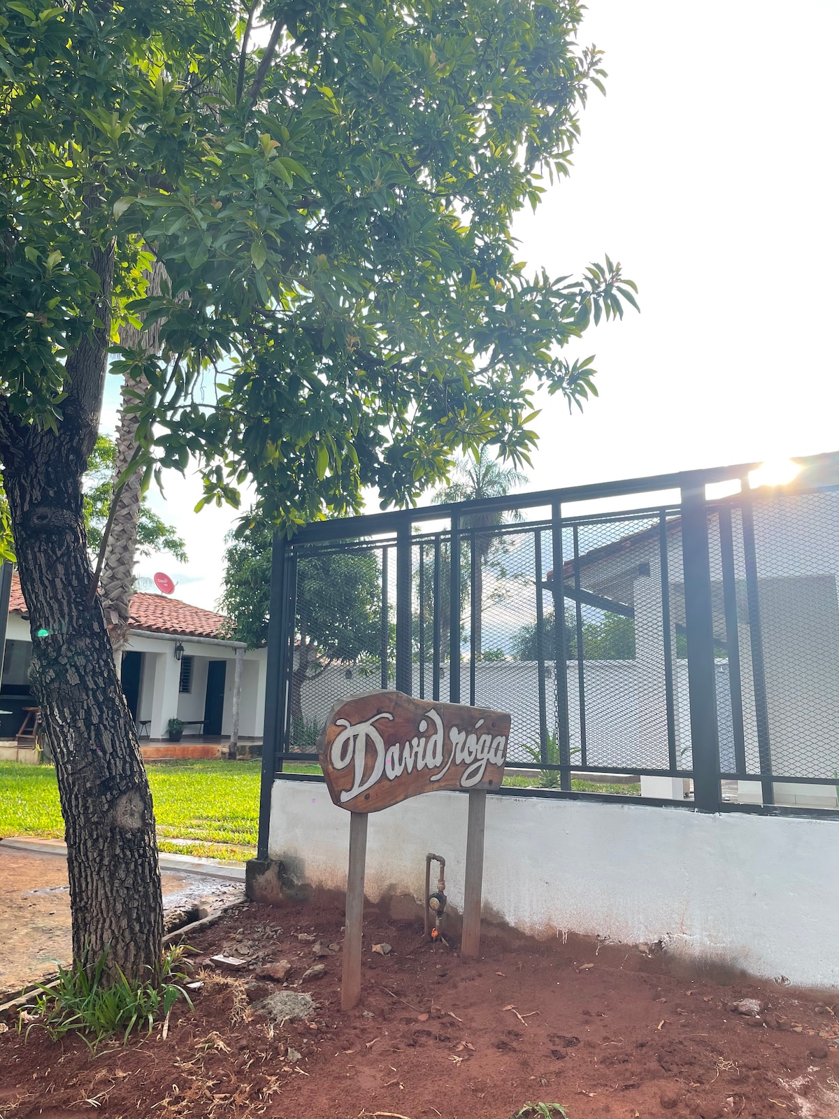 A sign with the name 'David' is positioned near a tree, indicating the entrance to the property. The surrounding area features green grass and a pathway leading up to a building visible in the background.