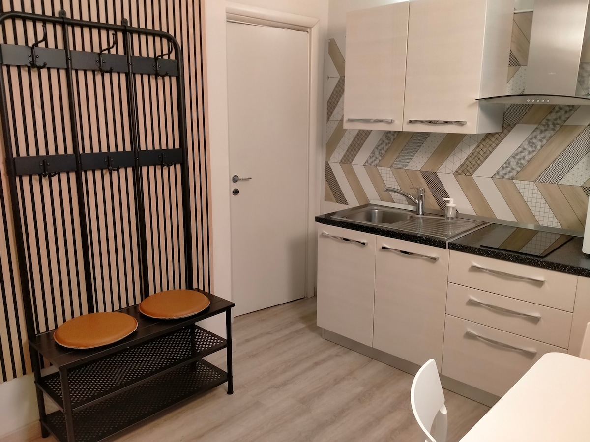 A modern kitchen area is featured, showcasing light-colored cabinetry and a well-maintained countertop. A wall-mounted coat rack stands adjacent to a stylish seating bench with two round cushions. The patterned backsplash adds a subtle design element to the space.