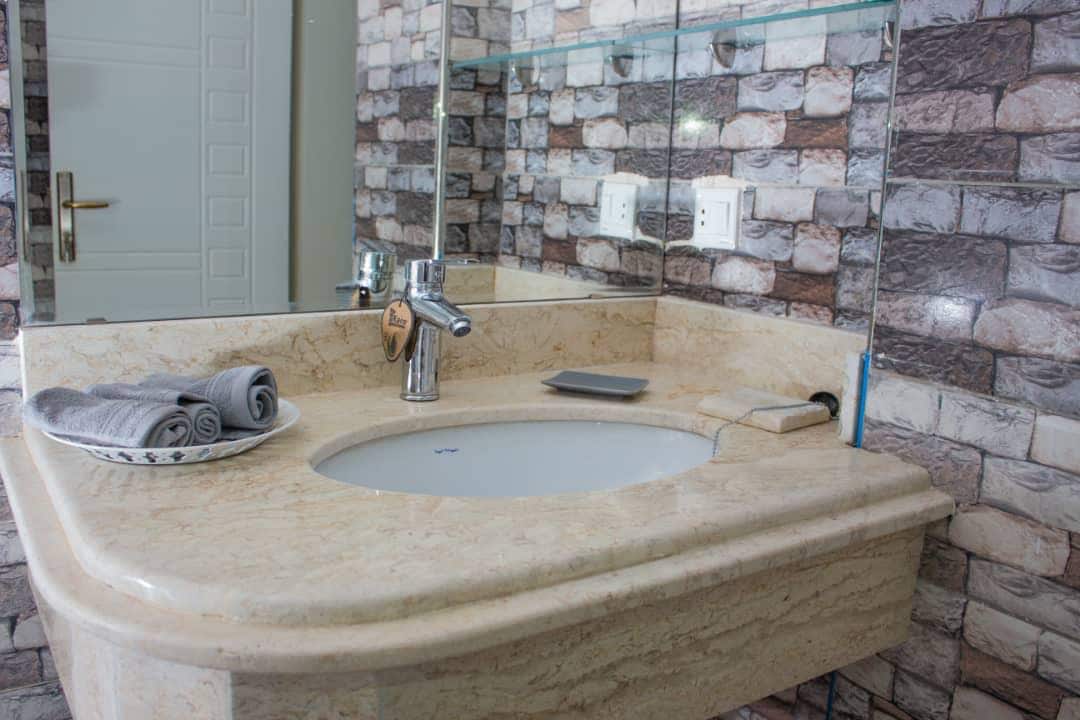 A well-appointed bathroom features a marble countertop with an integrated basin. Fresh towels are neatly rolled on a decorative plate. The walls are adorned with a stylish brick-patterned finish, providing a modern touch to the space. Lighting enhances the bright and clean appearance.