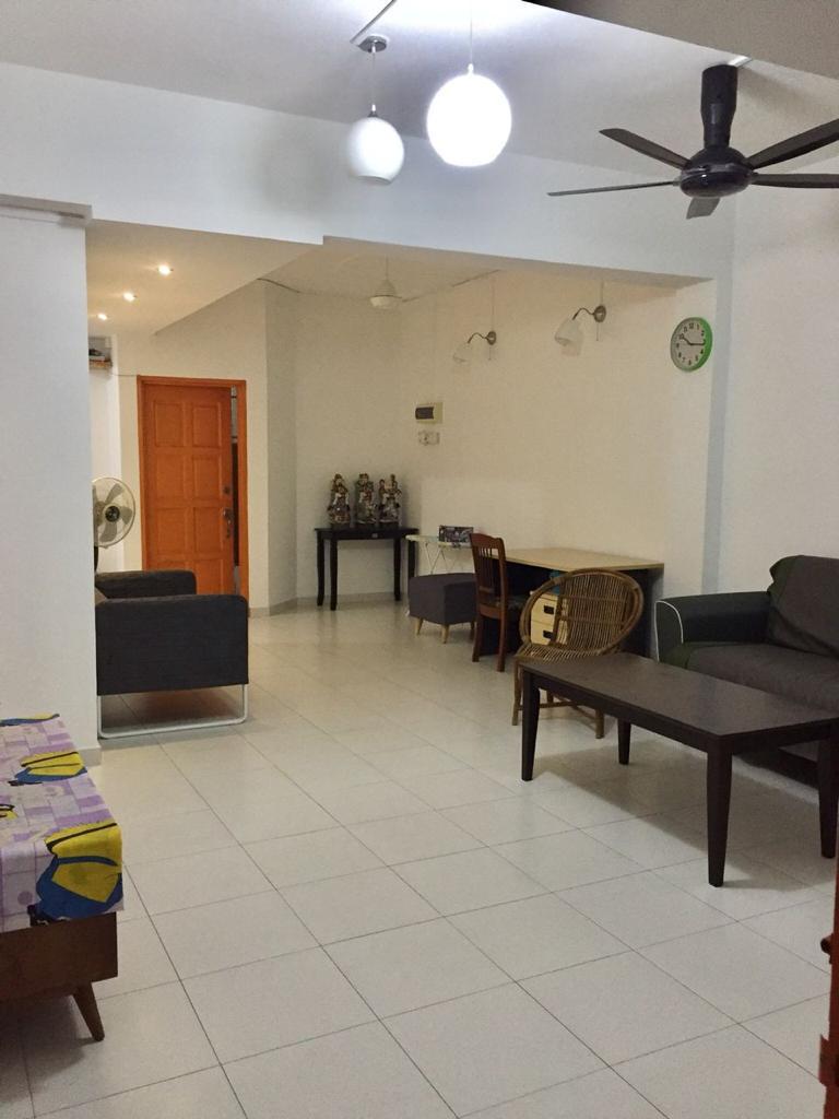 An open living space features white tiled flooring and a ceiling fan. Two seating areas are provided, one with a dark green couch and another with grey furniture. A small wooden table and chairs are visible, along with a decorative clock on the wall.