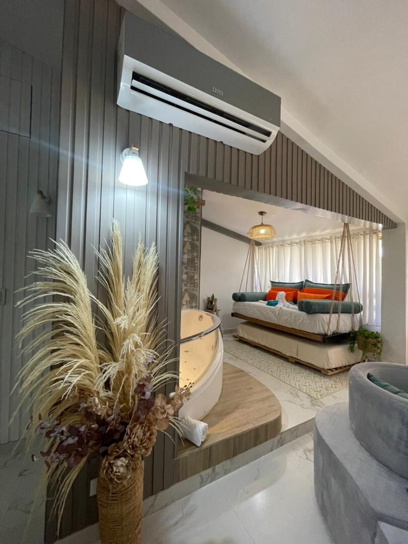 A modern living space is highlighted by a wooden accent wall and gentle lighting. A cozy seating area with colorful cushions invites relaxation. A decorative plant arrangement adds a touch of nature, while a swing chair enhances the unique design of the room.