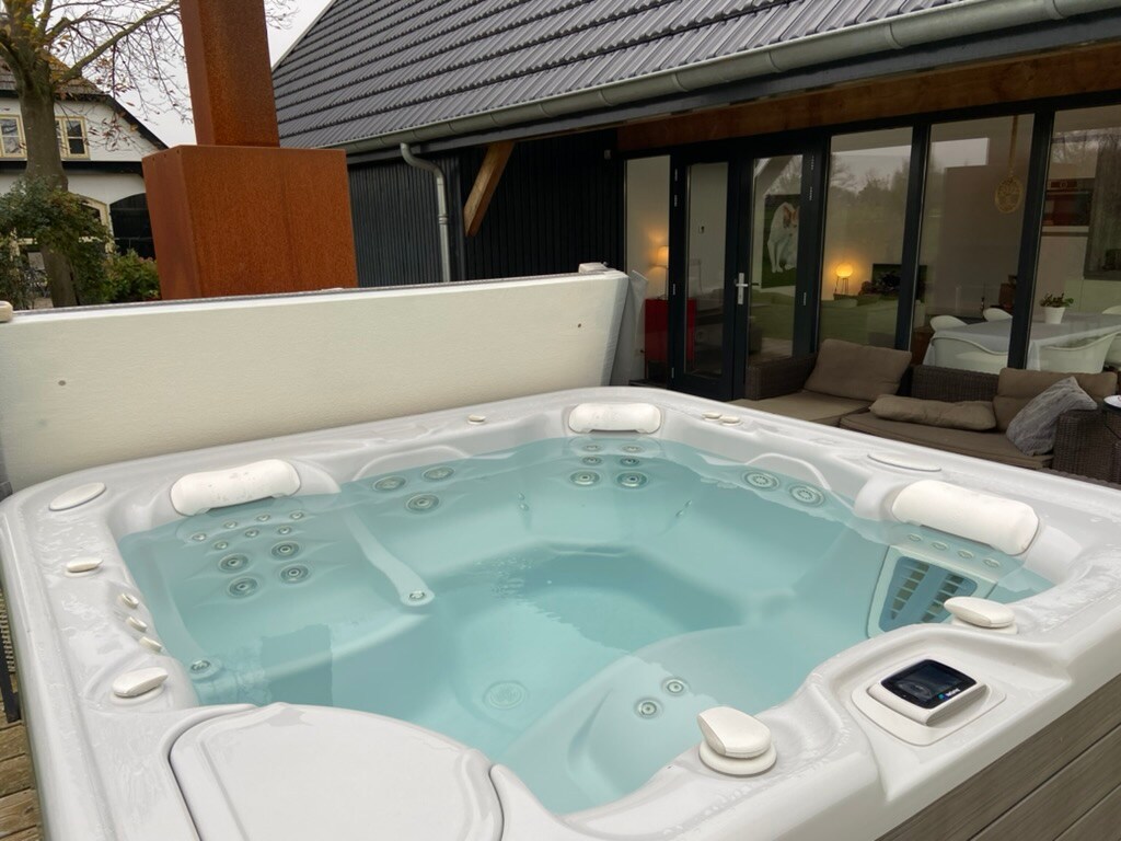 A modern jacuzzi is positioned on the terrace, featuring multiple seats and adjustable jets. The clear water reflects natural light, creating a peaceful atmosphere. In the background, French doors provide access to the spacious living area, enhancing the connection between indoor and outdoor spaces.