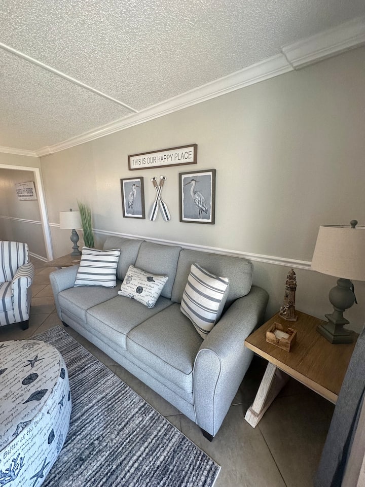 Sebule ya kondo ya ghorofa ya chini inatoa viti vyenye nafasi kubwa na sofa ya kulala, inayofaa kwa ajili ya kupumzika. Milango mikubwa inayoteleza inaelekea moja kwa moja ufukweni, ikitoa mandhari ya kupendeza na ufikiaji rahisi. 