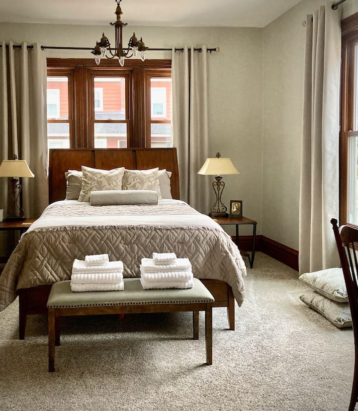 More of the home's beautiful wood abounds in the first-floor bedroom, with a desk (right corner of photo), TV, and original fireplace at bottom left of the bed.
