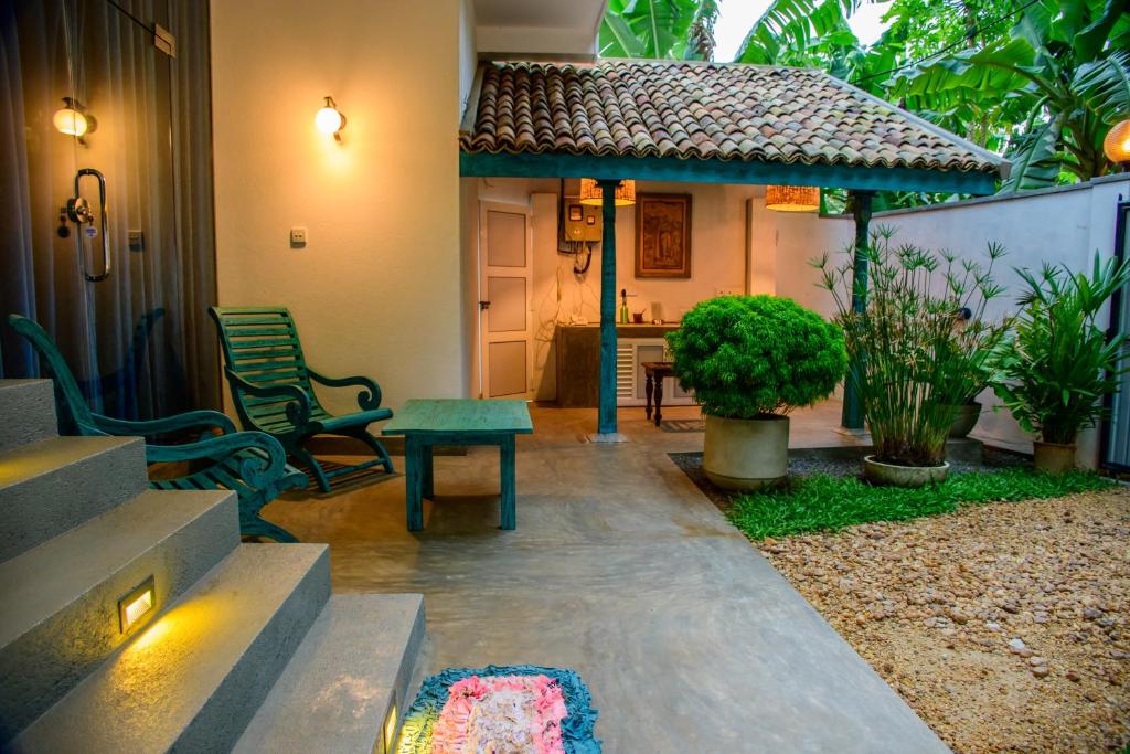 An inviting outdoor area features a small table and chairs, surrounded by lush greenery. A covered patio offers shade, while stone steps lead to the entrance of the guest house. Decorative potted plants add a touch of nature to the setting.