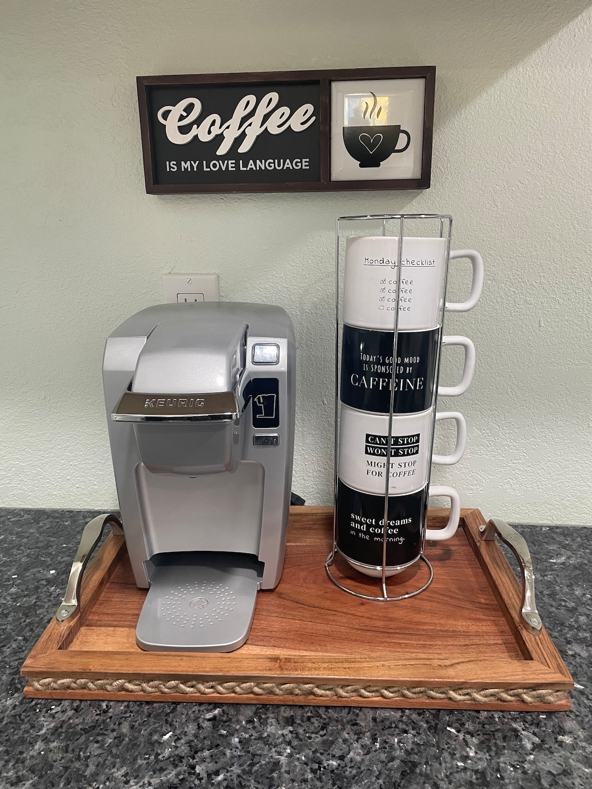 A sleek coffee maker is displayed on a wooden tray, accompanied by a stack of three coffee mugs. A decorative sign above reads 'Coffee is my love language,' contributing to a cozy kitchen atmosphere.