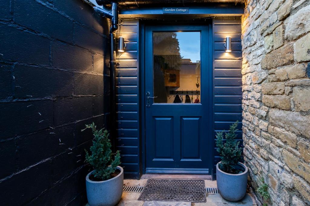 An inviting entrance features a dark blue door set within a stone and black-painted wall. Two potted plants are positioned on either side of the door, and warm lighting enhances the doorway, creating an entrance that welcomes guests.