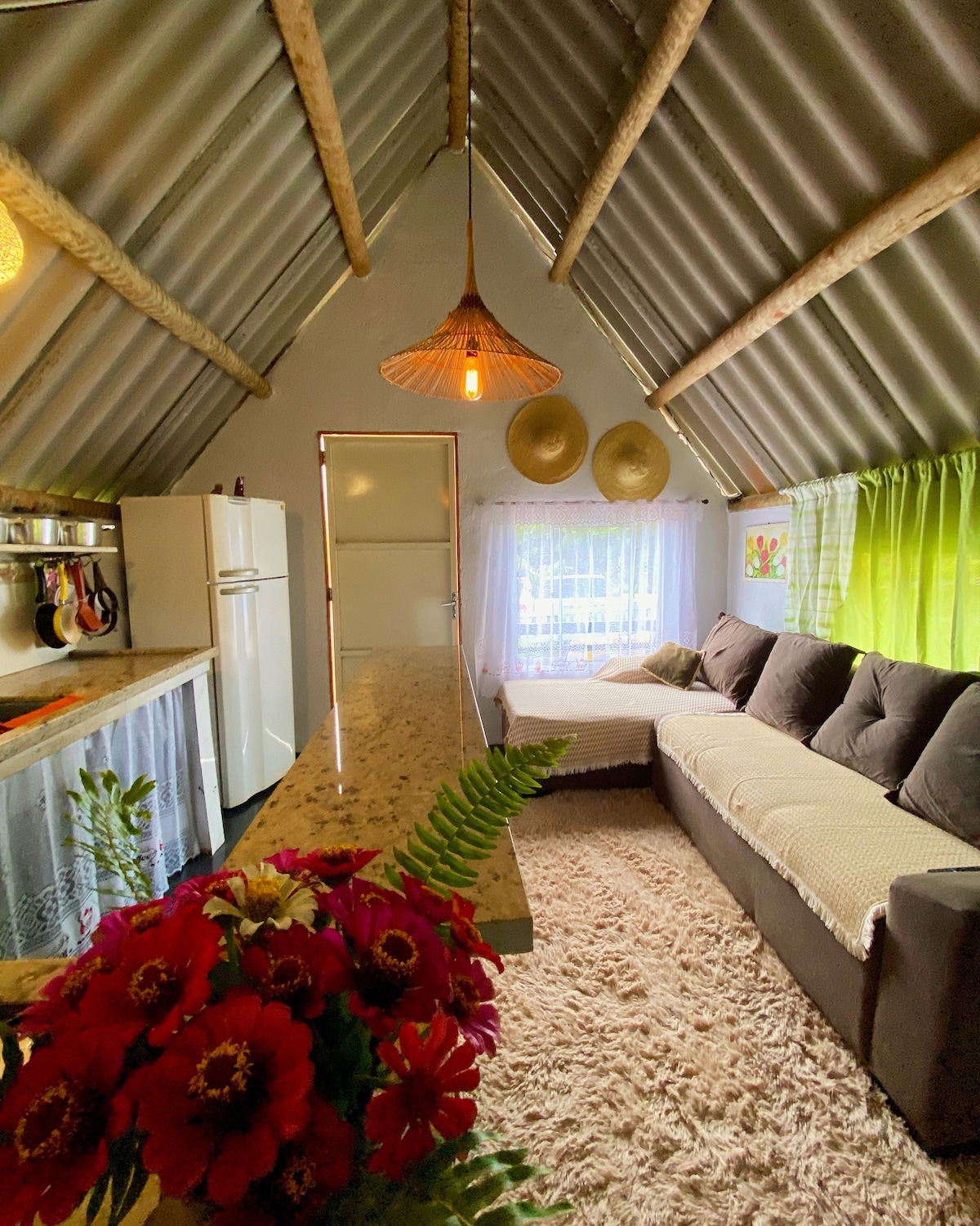 A cozy living area features a modern kitchen with a marble countertop and stainless steel appliances. A plush sofa with neutral cushions sits against the wall, complemented by a decorative rug. Natural light filters through sheer curtains, and decorative wall art adds warmth.