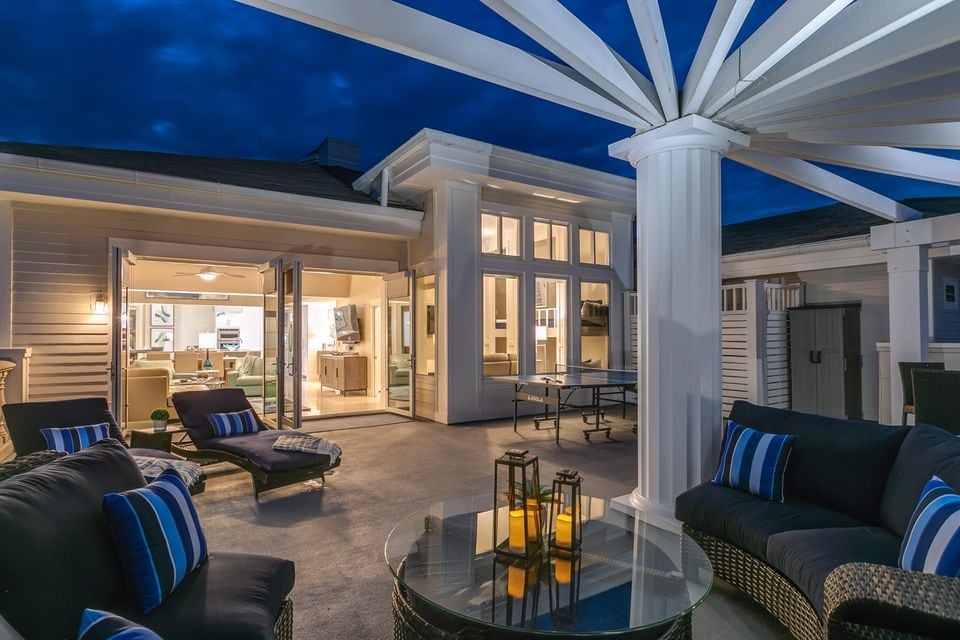 An expansive private terrace is adorned with lounge chairs and seating areas. The pergola's beams extend overhead, creating a distinctive architectural feature. Soft lighting from lanterns highlights the outdoor space, while large glass doors provide a view into the penthouse's interior.