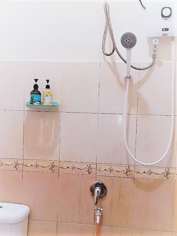 The bathroom features a showerhead mounted above a sleek tiled wall, with a small shelf displaying liquid soap and shampoo. A modern shower control is positioned near the floor, adjacent to a toilet, ensuring essential amenities are within reach.