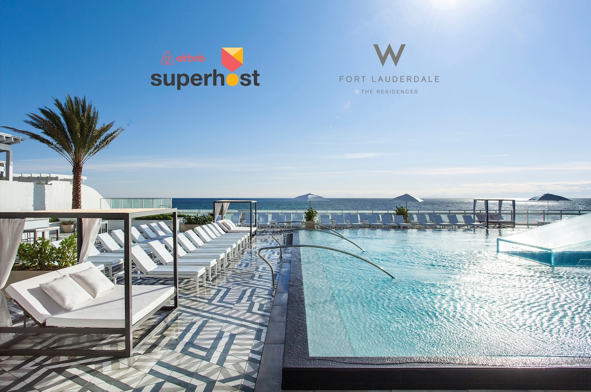 An outdoor pool area features sleek lounge chairs arranged on a sun-drenched deck beside a shimmering infinity pool. The ocean horizon stretches in the background, complemented by clear skies and palm trees swaying gently.