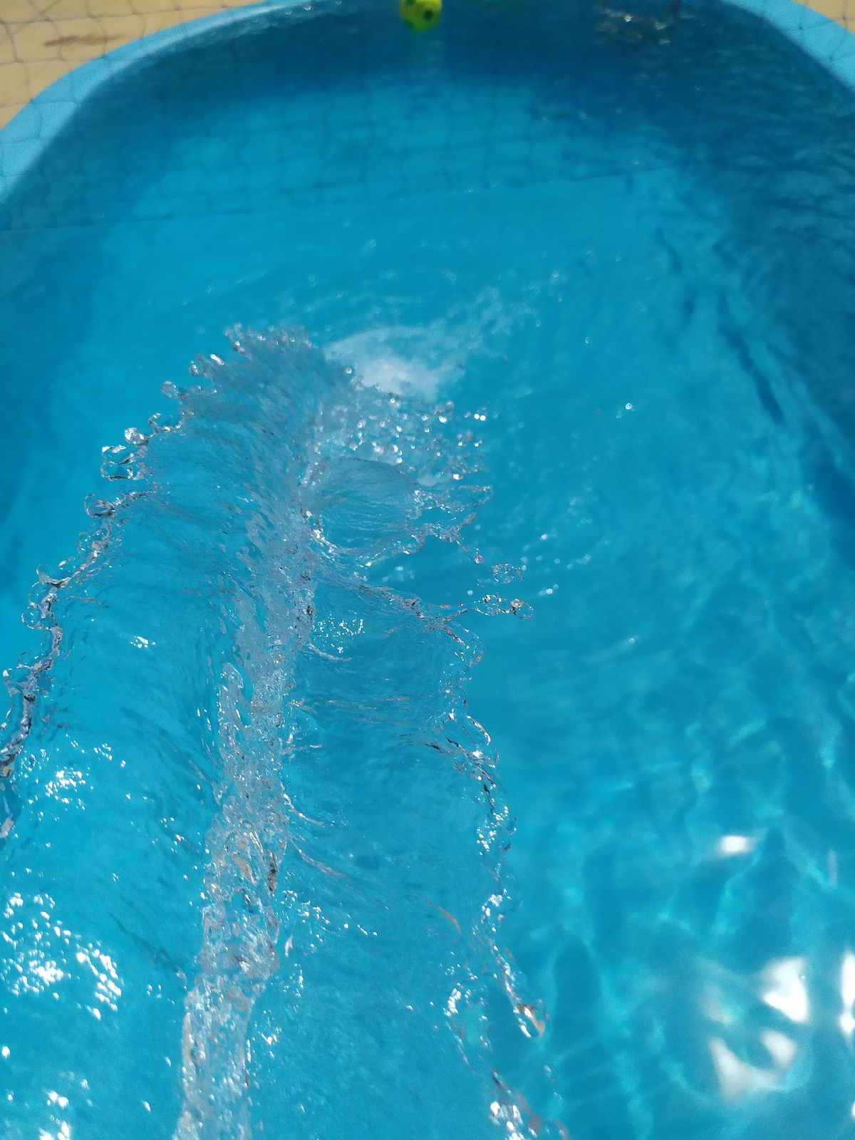 The image captures clear blue water in a swimming pool, with gentle ripples forming across the surface. A small fountain feature is visible, creating a stream of water that adds movement and clarity to the tranquil ambiance.