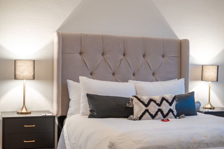 سرير بحجم كوين في غرفة الضيوف مصمم بشكل مثالي مع بياضات بيضاء فاخرة.