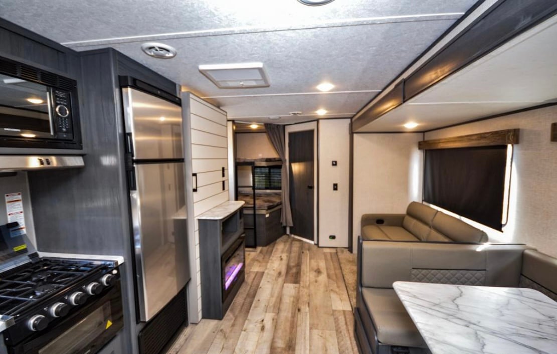An inviting interior of a modern camper is showcased, featuring a fully equipped kitchen area with a gas range and microwave. A spacious seating area is complemented by a marble-top dining table. Soft lighting enhances the ambiance, while stylish decor adds to the overall comfort.
