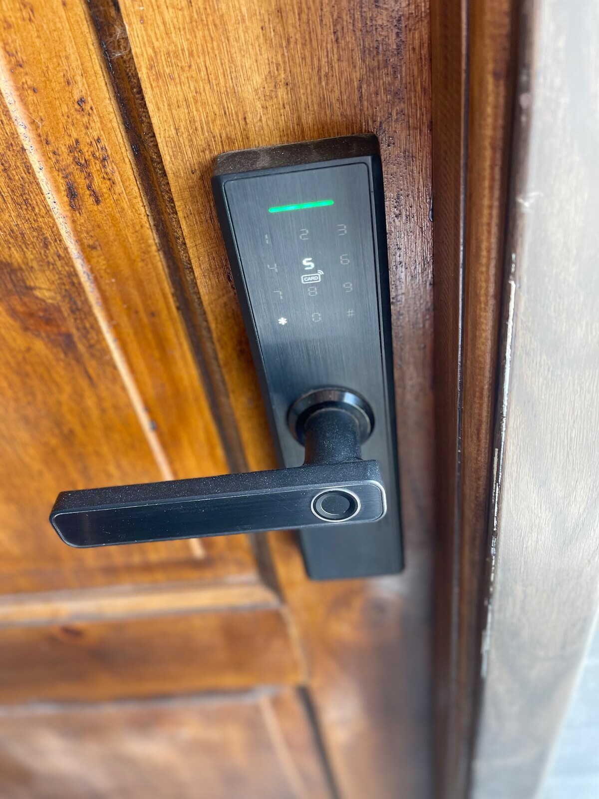 A modern digital keyless entry system is installed on a wooden door. The sleek handle is complemented by a numeric keypad, featuring a green light indicator. The rich texture of the wood contrasts with the streamlined design of the lock interface.