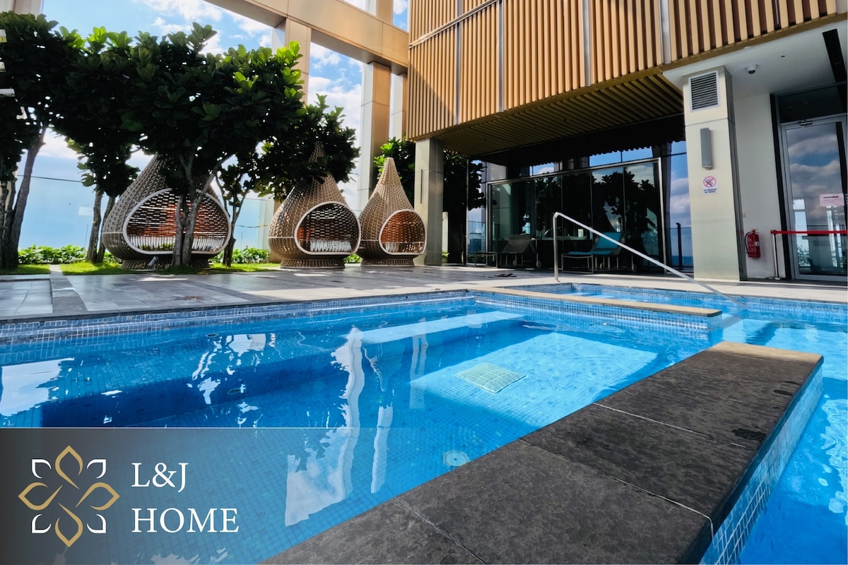 A modern pool area is presented with a clear blue water feature reflecting the sky. Comfortable hanging chairs are positioned nearby, surrounded by greenery. The clean, sleek design is enhanced by stylish architectural elements, providing a serene ambiance for relaxation.