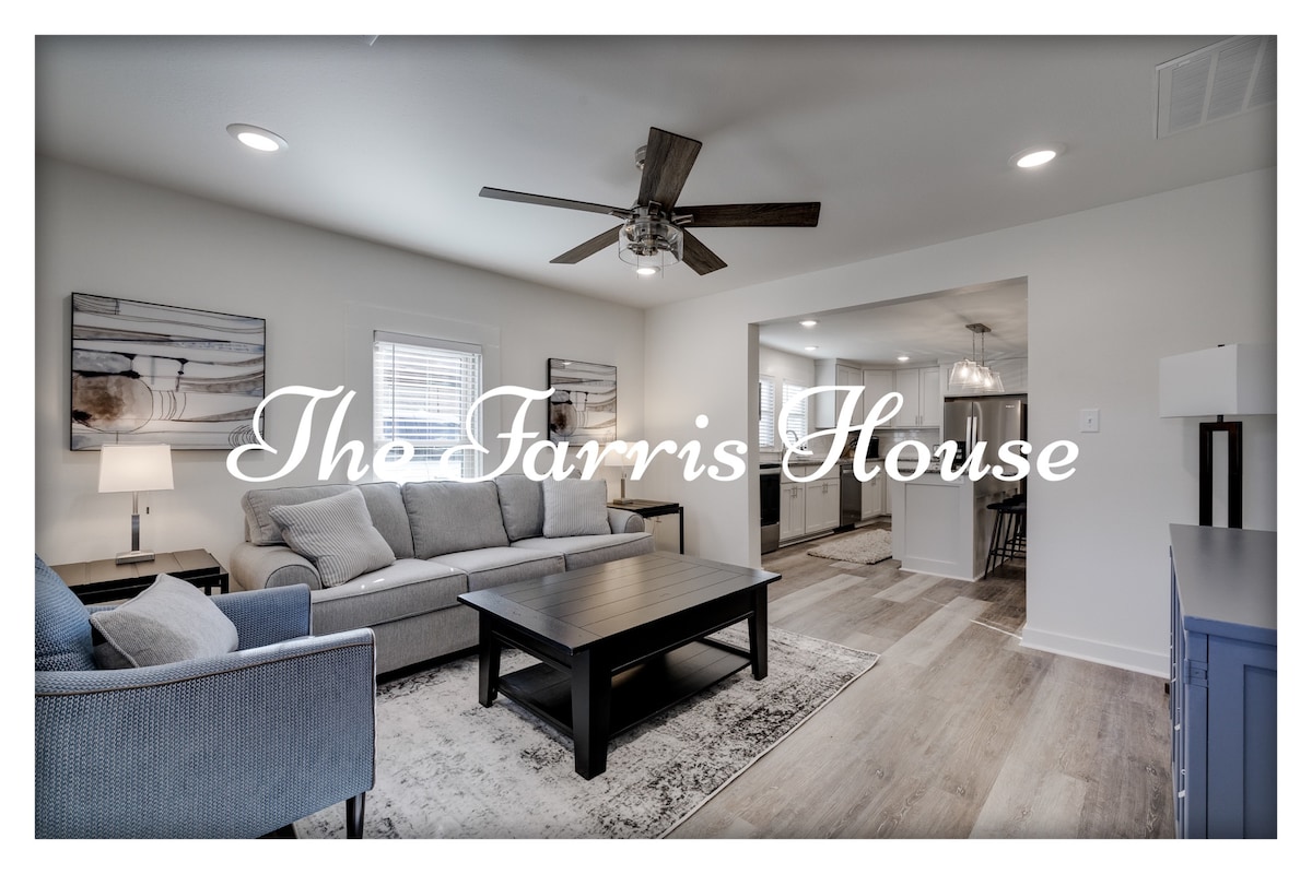 A living area is highlighted by a light gray sofa flanked by two accent chairs. A dark coffee table sits in the center, with artwork hanging on the walls. Soft lighting is provided by a floor lamp and recessed ceiling lights, creating an inviting space.