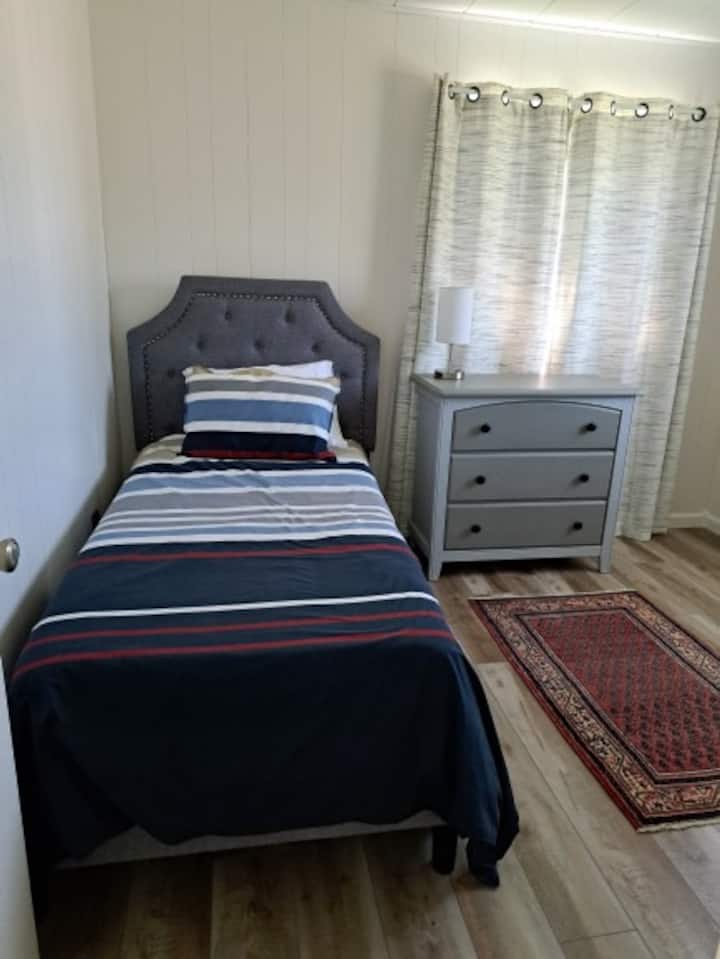 This single bedroom is a corner room with  two windows to keep it sunny and bright. It includes a dresser and clothes rack to store your things. Blackout curtains darken the room for a good night's rest.