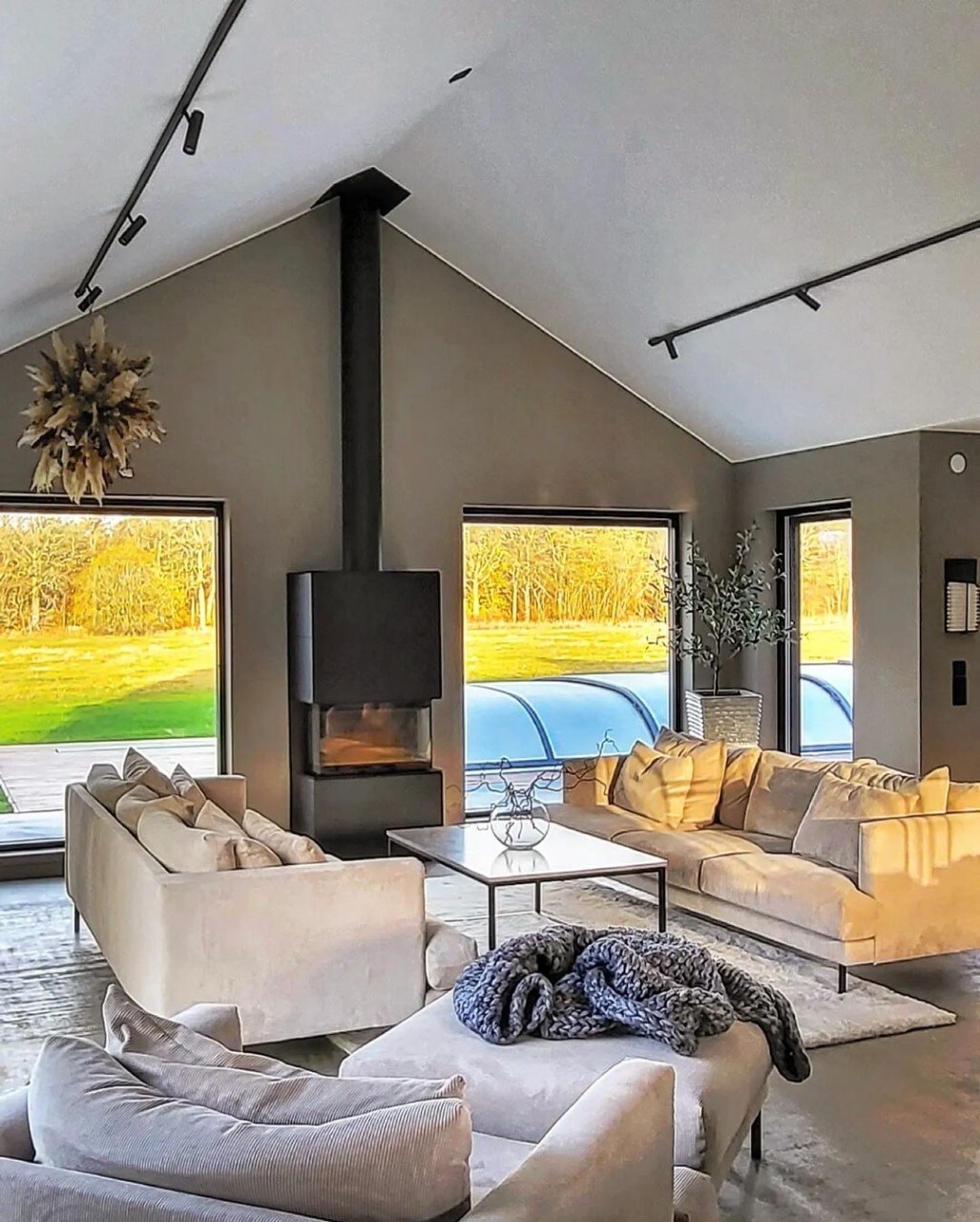 A modern living area features large windows that fill the space with natural light, providing views of the surrounding landscape. Comfortable sofas are arranged around a central coffee table, with a minimalistic fireplace adding warmth to the inviting environment.