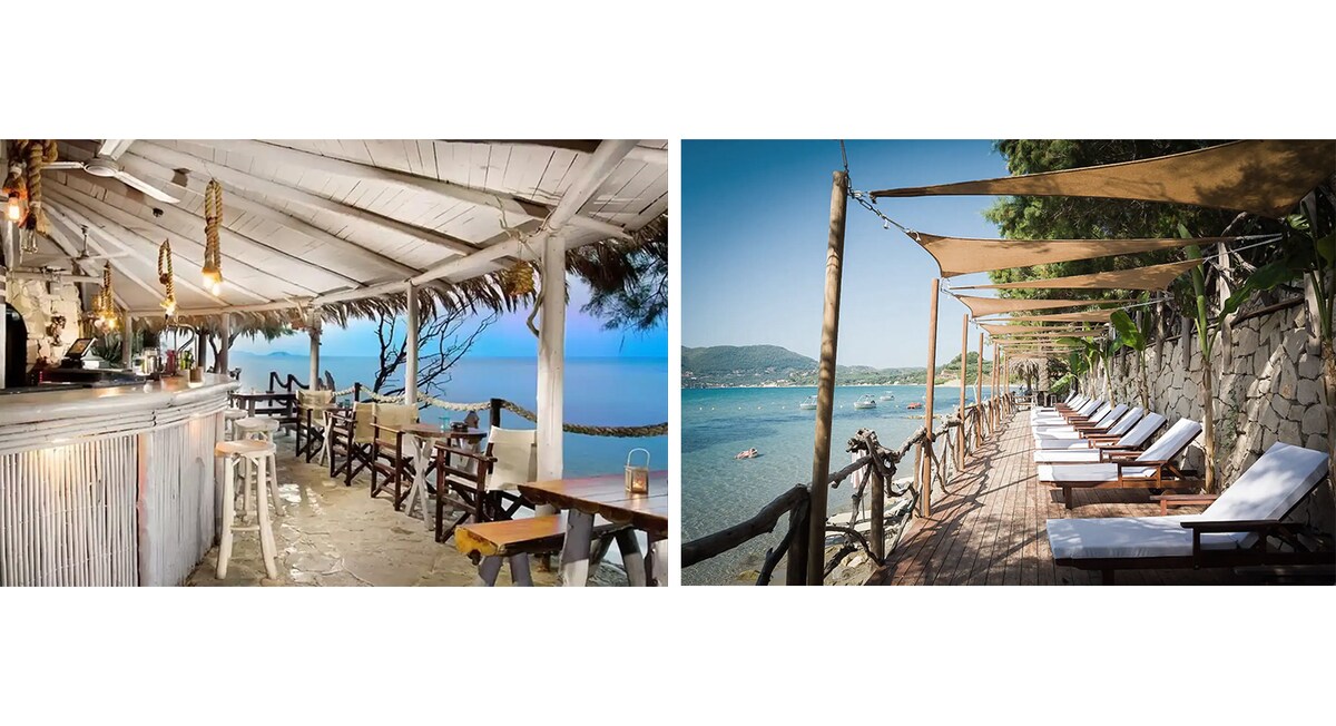 An open-air beach bar features rustic wooden furniture beneath a thatched roof, offering a panoramic view of the sea. Sun beds are arranged along a sandy shore with umbrellas providing shade, while the calm waters invite relaxation and leisure.