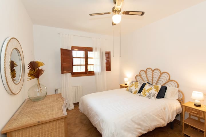 Este primer dormitorio está completamente amueblado con bambú natural. La cama es de 160x190. La cama y el colchón son de 2023 de la marca Pikolin. Un ventilador de techo y una gran ventana permiten disfrutar de una habitación fresca para dormir.