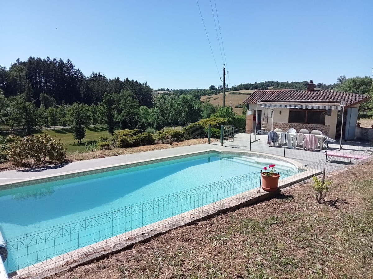 A tranquil swimming pool is framed by a well-maintained patio and surrounded by lush greenery. Nearby, a spacious outdoor dining area is visible, equipped with multiple tables and chairs. The beautiful landscape includes trees and rolling hills in the background, creating a serene atmosphere.