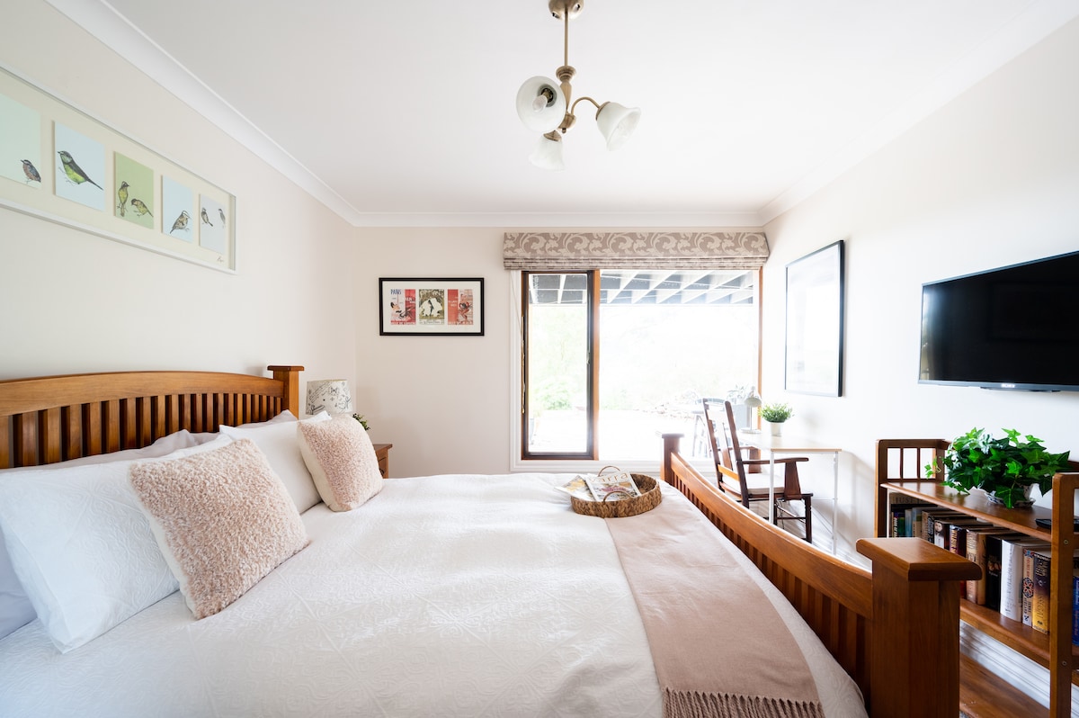 Dormitorio con cama tamaño queen y vistas al jardín de arbustos. Televisión a pie de la cama para mayor comodidad de los huéspedes y escritorio.