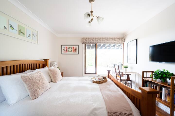 Спалня с двойно легло и изглед към храстовата градина. Телевизор в подножието на леглото за комфорт на гостите, плюс бюро.