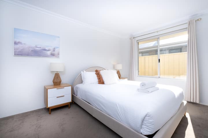 Chambre lumineuse et accueillante avec un lit queen size avec des draps moelleux, complétée par des tables de chevet élégantes et des lampes. Une grande fenêtre remplit la pièce de lumière naturelle, et l'art mural serein ajoute une touche apaisante.